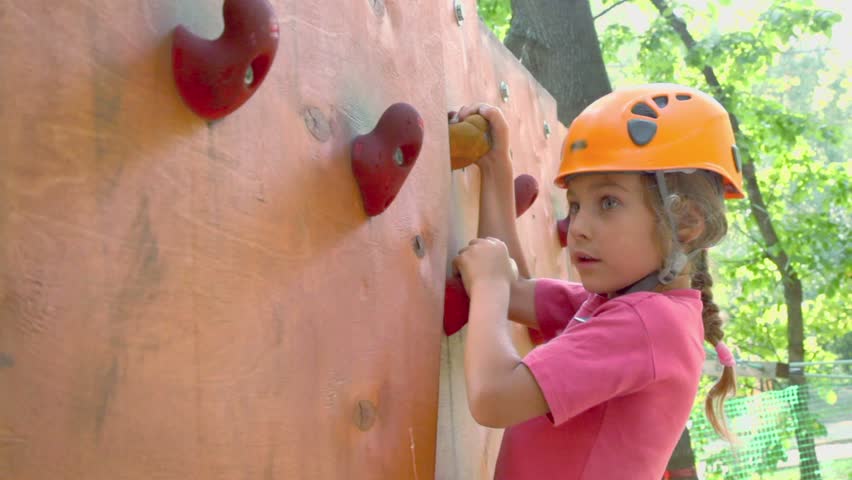 Rock climbing. Little girl in helmet crawls on pendant wall in outdoor climbing center, closeup Royalty-Free Stock Footage #3418931