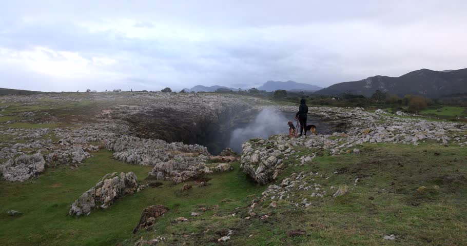 Young woman with two dogs at Bufones de Pria blowhole in Spain on Atlantic coast on a cloudy day