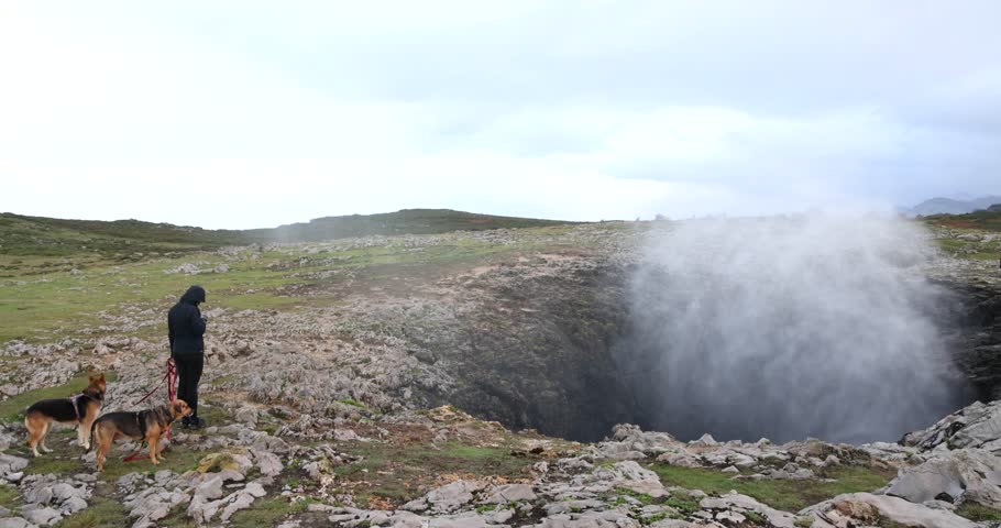 Young woman with two dogs at Bufones de Pria blowhole in Spain on Atlantic coast on a cloudy day