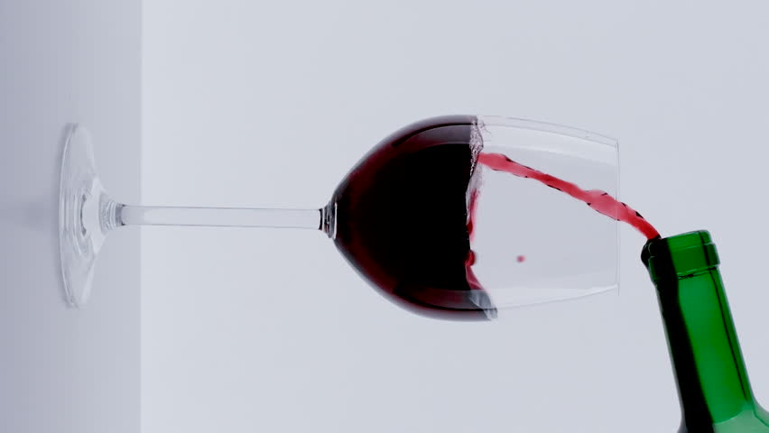 Red wine forms beautiful wave. Wine pouring in wine glass over white background. Close-up vertical shot for social media tik-tok 
instagram, Slow motion of pouring red wine from bottle into goblet.