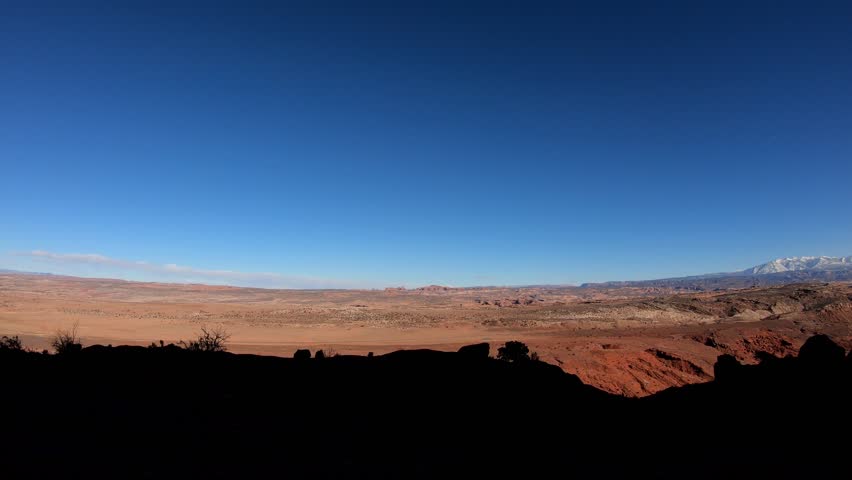 A side perspective with dark shadows as the sun sets; revealing the stark contrast of the rugged Gemini Bridges Trail and the modern highway.