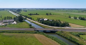 Red and White Train Crossing Small Bridge Over a Canal, Stationary Shot - Friesland, The Netherlands, 4K Drone Footage

