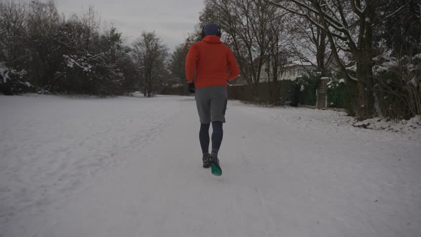 Male jogger running on snow in winter in orange sweatshirt back view. People daily outdoor active lifestyle. Enjoying sport. Rear view of man trail running in winter. Run in freezing snowy weather.  Royalty-Free Stock Footage #3419202299