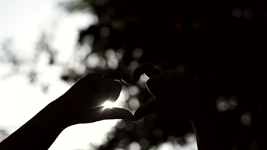 Man hands making shape of heart over abstract nature bokeh background,slow motion shot.