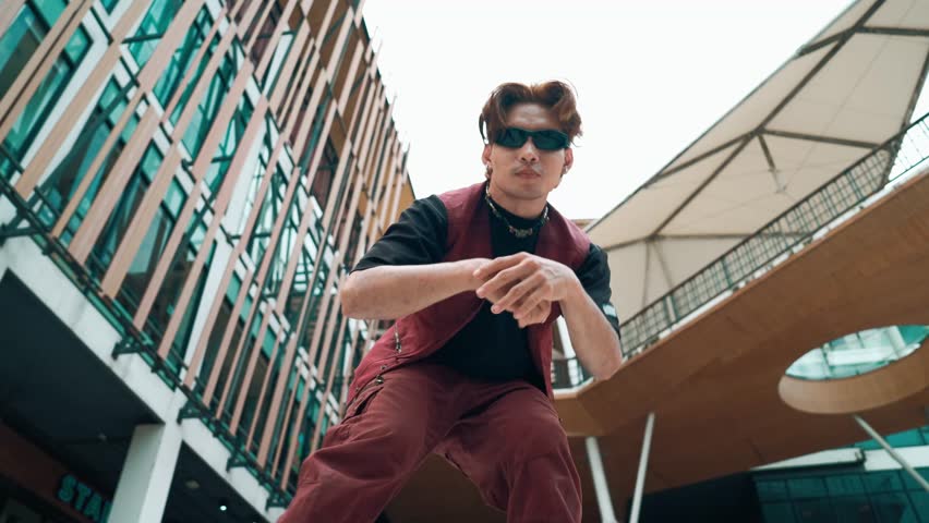 Low angle of asian attractive hipster pose at camera surround by mall. Happy break dance choreographer looking at camera while dancing in hip hop style. Hip-hop culture. Outdoor sport 2024. hiphop.