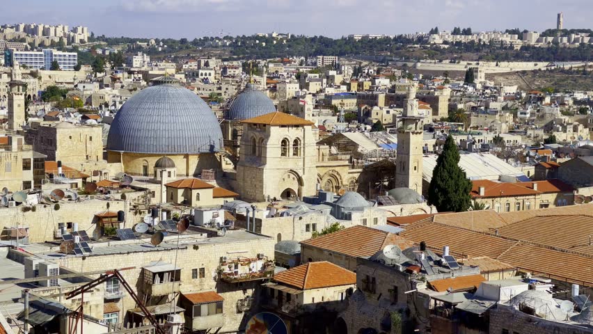 Pan right scenic view of old historic temples and churches located in ancient Jerusalem district with buildings and green trees under cloudy sky