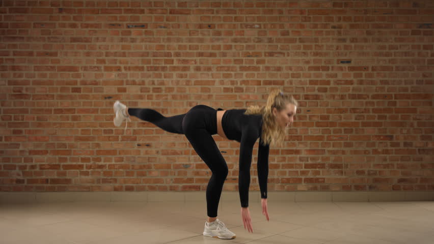 One leg Romanian deadlift. A trainer skillfully demonstrates how to perform the exercise, one leg Romanian deadlift. A girl in good physical shape. She is in black sportswear in a loft gym. 8K RAW.