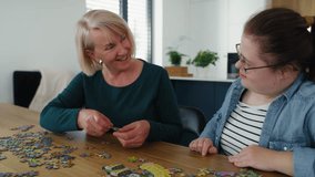 Joyful down syndrome woman and her mother assembling puzzles at home