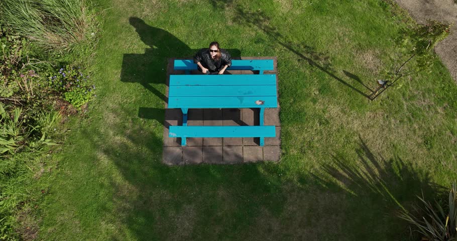 A woman sits at a blue wooden table and has a great time in nature 4k