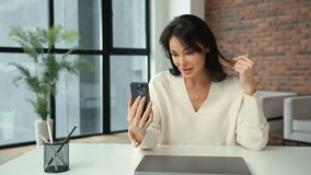 Engaged and cheerful, a businesswoman communicates on a video call via her smartphone, her office desk providing a professional backdrop. Camera 8K RAW. 