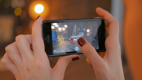 MOSCOW, RUSSIA - DECEMBER 10, 2017. Woman using smartphone with augmented reality app and placing virtual furniture in room. Future and technology concept. Christmas holiday bokeh background