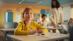 Portrait of a Cute Smiling Redhead Girl Sitting Behind a Desk in Class in Elementary School. Young Pupil is Looking at Camera, Smiling. Kids Educated in Modern Primary School - Powered by Shutterstock - Get 15% off with code: PIKWIZARD15