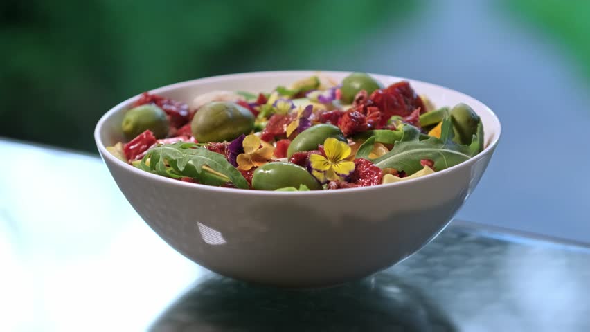 Pouring olive oil and balsamic vinegar on fresh salad with lettuce leaves, sun-dried tomatoes, mozzarella cheese, capers and olives. Healthy food concept. Dressing summer salad with oil