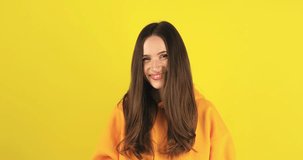 Happy brunette woman having mobile video call, wave hands and say hi, hello isolated on yellow background. Nice to see you. Happy emotions. Beautiful young girl speaking video call online smartphone.