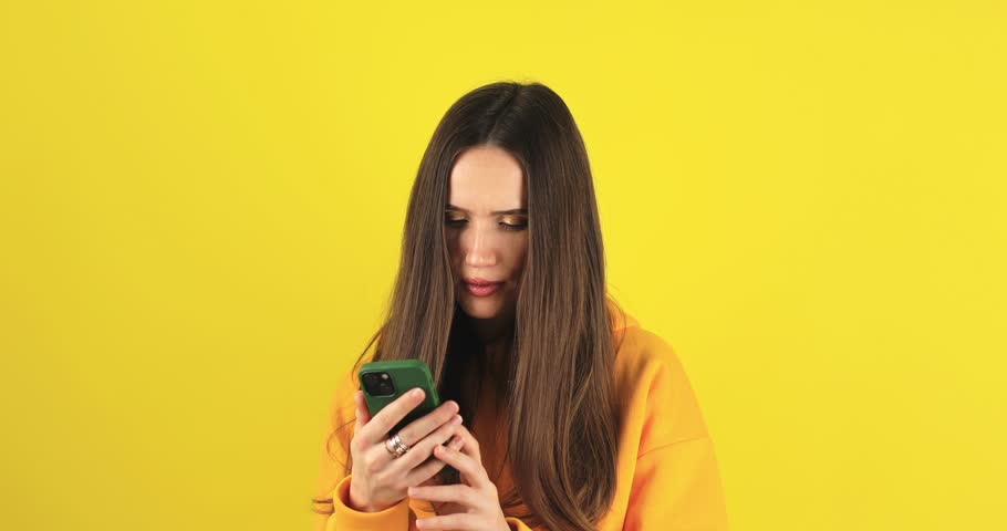Close up brunette woman touch face, pensive think problem solution looking at mobile phone. Thoughtful girl thinking idea browsing smartphone chat isolated yellow background, woman not sure. Royalty-Free Stock Footage #3419566261