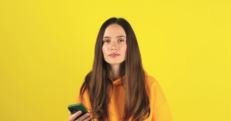 Close up brunette woman touch face, pensive think problem solution looking at mobile phone. Thoughtful girl thinking idea browsing smartphone chat isolated yellow background, woman not sure. Royalty-Free Stock Footage #3419568589