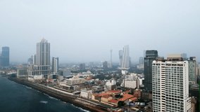 Aerial view of Colombo skyline, displays urban density, skyscrapers, oceanfront developments in Sri Lankan capital. Video showcases cityscape, coastal roads, architecture for urban planning, travel.