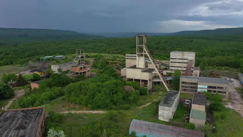 Aerial drone view of old abandoned overgrown coal mine. The shaft tower and desolate concrete buildings of mining factory. Decarbonization, green deal in the modern world during the energy crisis.
