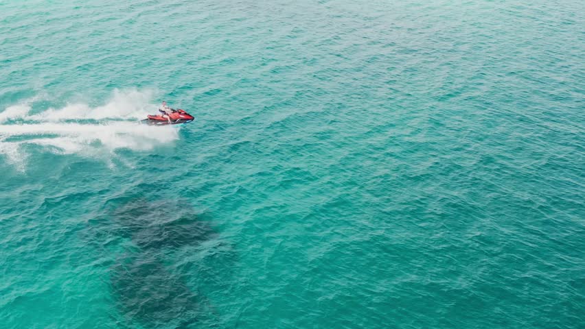 Person riding jet ski at high speed on blue water, Maldives. Aerial follow