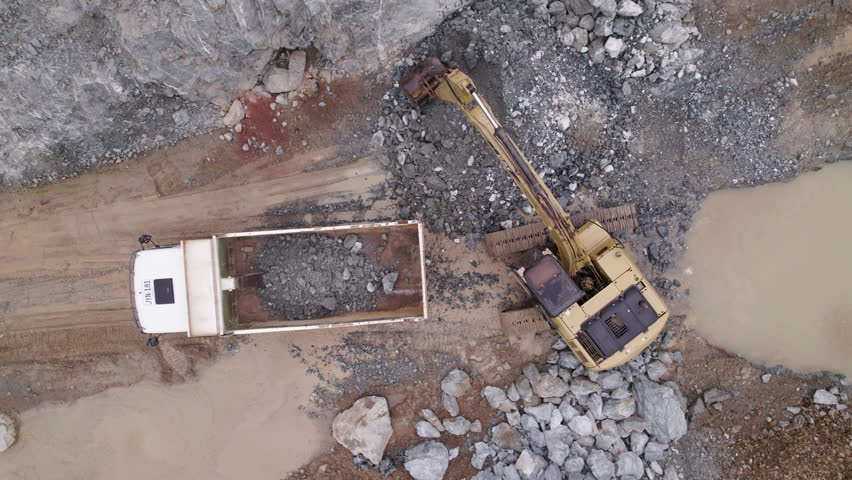 A dynamic drone shot of a excavator which empties its yield into a mining truck