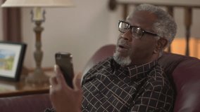 A happy elderly African American grandpa smiling and waving, chatting on a smartphone. Authentic family feel. Prores file.