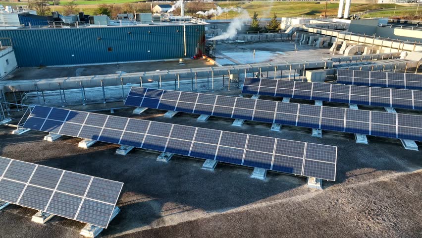 Rows of solar panels in an industrial setting. Aerial establishing shot of industrial rooftop during golden hour sunset.