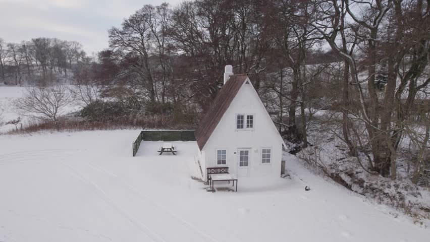 Cottage House Under The Snow By the Shore of An Icy Fjord - Aerial Shot