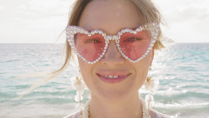 Super positive girl with good energy sending big air kiss to camera. Portrait smiley woman in fancy heart shape pink glasses checking her style and flower earrings. Close up happy emotional bride face Royalty-Free Stock Footage #3419896647