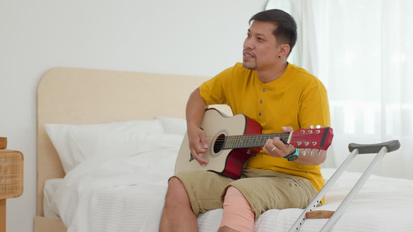 asian man smiling and playing guitar on the bed