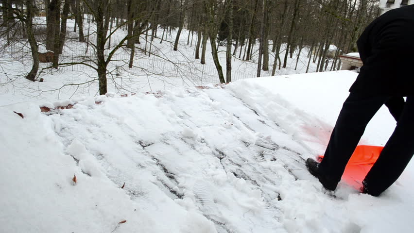 man in black with plastic orange shovel tool clean snow from roof in winter.
