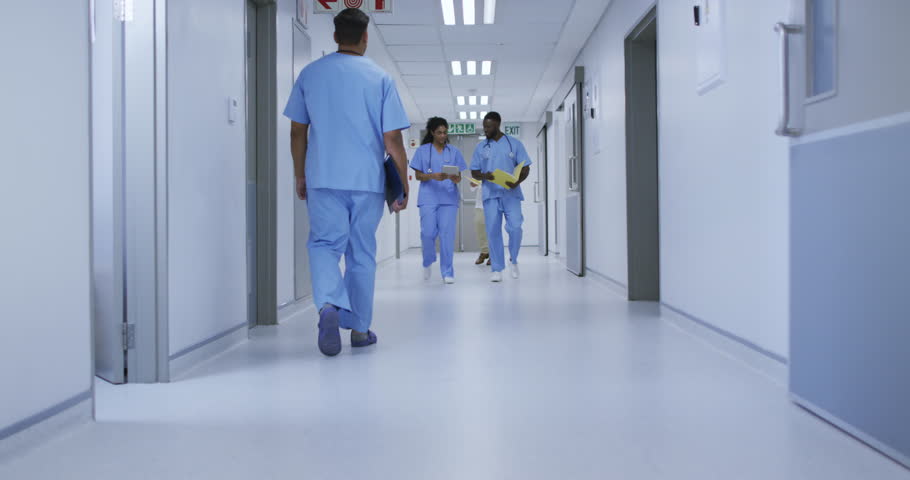 African american male and female doctor in discussion walking in busy hospital corridor. medicine, health and healthcare services.