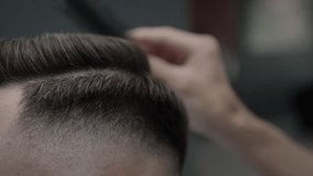 A male hairdresser combs the hair of a young caucasian male client with a comb after a haircut. Professional fashionable haircut in a barbershop. Slow motion, close-up