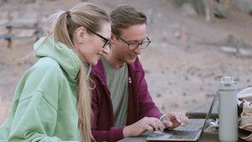 A joyful white couple shares a light moment as they work on a laptop in an outdoor setting, embodying a relaxed work vibe. Slow Motion. Camera 4K RAW.  - Powered by Shutterstock - Get 15% off with code: PIKWIZARD15