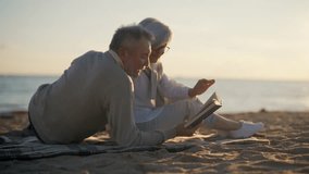 Senior gray haired man woman reading book together sitting hugging on sandy sea beach at sunset. Happy marriage, old family spending enjoy time, back view. Love relationship, resting concept. - Powered by Shutterstock - Get 15% off with code: PIKWIZARD15