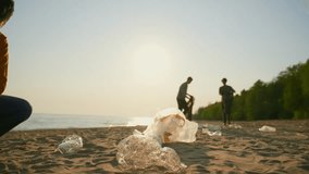 Group of volunteers collecting trash garbage on sandy sea shore in plastic bags at sunset. Ecology environment pollution and protection. Recycling of trash, rubbish, junk concept. Blur video.
