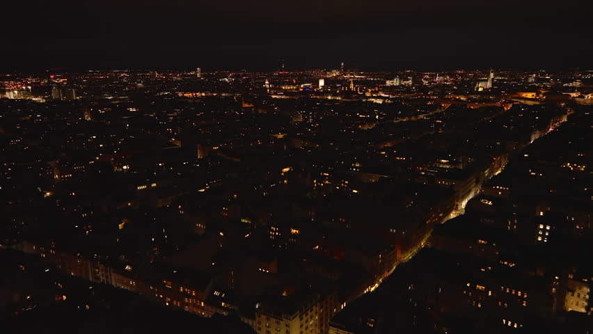 Forwards fly above buildings in urban borough at night. Dimmed town and blinking lights on high rise towers in distance. Vienna, Austria