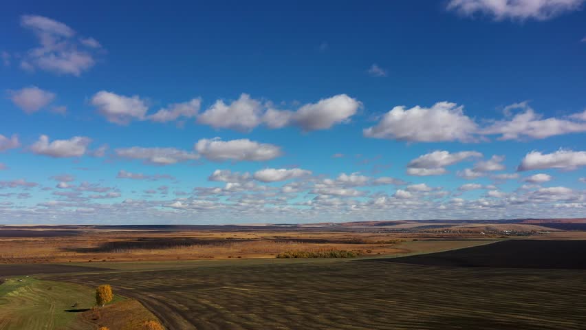 The drone flies high above the arable lands and farmland on a sunny autumn day