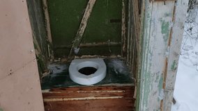 Man in a winter setting closes the door to an old village toilet and leaves. First person view video