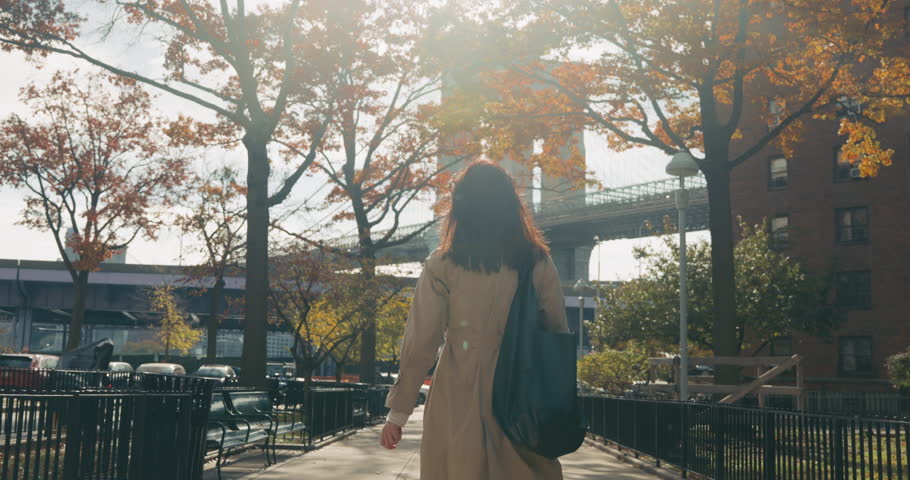 Rear view of stylish brunette female walking towards the iconic Brooklyn Bridge in the warm autumn glow of New York