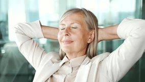 Elderly senior gray haired businesswoman relaxing with her eyes closed in an office. Calm happy female resting, took a break from work. Satisfied mature woman puts her hands behind her head. Close up - Powered by Shutterstock - Get 15% off with code: PIKWIZARD15