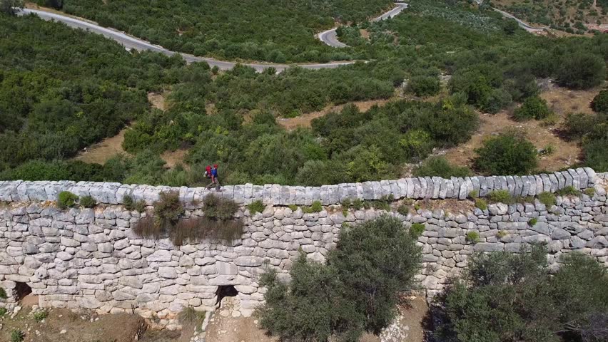 Steady drone shot of a hiker waling on top of a wall along the Lycian Way, a marked long-distance hiking trail in southwestern Turkey.