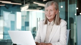 Elderly senior gray haired businesswoman typing on a laptop sitting at a workplace in office. Happy mature business female working in computer application, banking, texting a client, chatting online - Powered by Shutterstock - Get 15% off with code: PIKWIZARD15