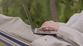 Close up video of woman working on laptop while sitting in hammock
