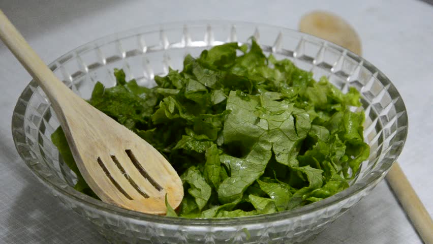 chef add spice and mix lettuce green salad in glass bowl with wooden spoon