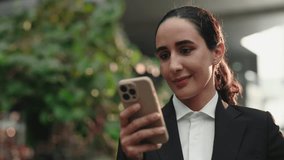 Positive Lady receiving Funny Video on Smartphone, Standing Outdoors in the Office Building. Beautiful Entrepreneur Reading Cool Sms on Cell Phone and Enjoy It. People and Technology Concept
