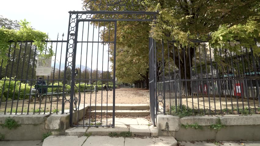 Walking through a metal gate into a park with leaves on the ground