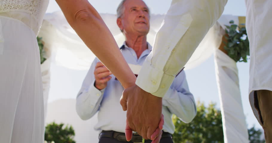 Caucasian bride and groom standing at outdoor altar with wedding officiant during ceremony. romantic summer wedding outdoors.