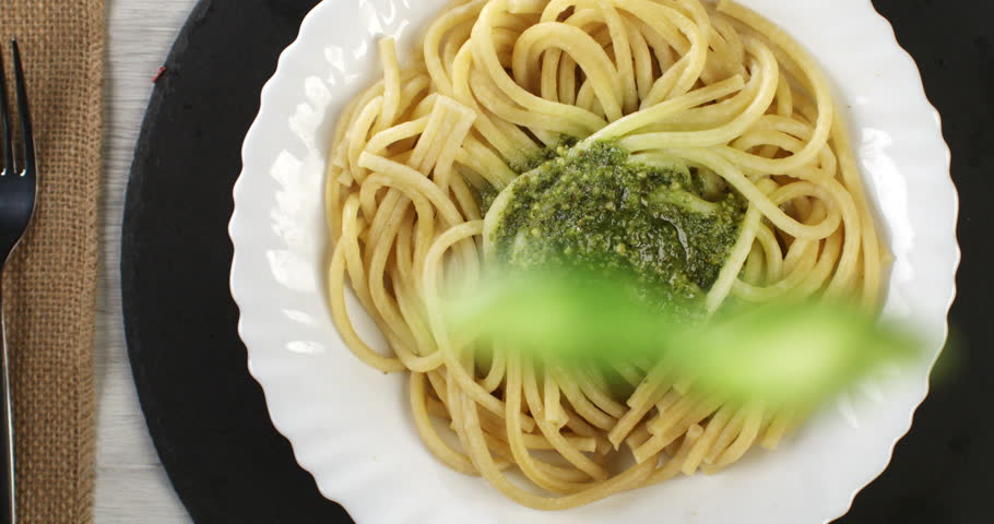 Super slow motion top view of fresh green basil leaf is falling on traditional italian dish of pasta spaghetti with pesto Genovese sauce with grated parmesan cheese at 1000 fps.