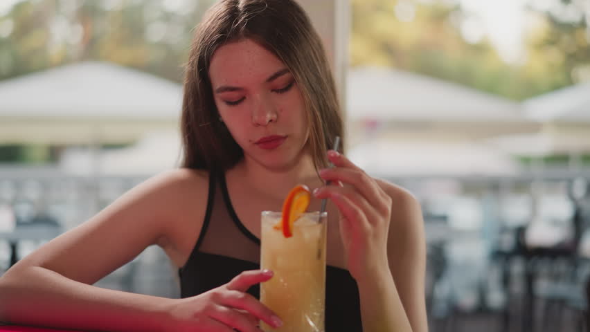 Bored lady with cocktail sits in bar. Young woman looks lonely resting in beach bar alone. Female guest drinks exotic beverage with orange slice Royalty-Free Stock Footage #3420447039