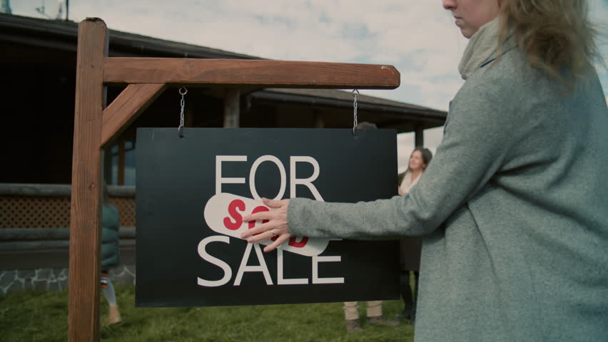 Female real estate agent puts sold sticker on for sale sign and congratulates young family with purchase. Realtor gives keys and goes to house with new owners. Residential property on sale concept. - Powered by Shutterstock - Get 15% off with code: PIKWIZARD15